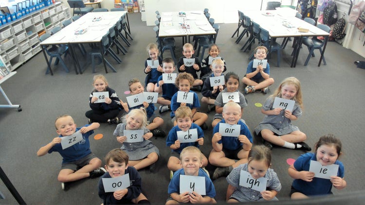 Students sitting on the floor in the classroom holding up spelling sounds