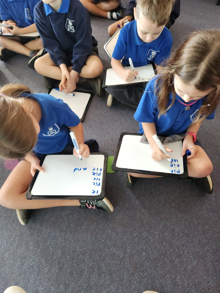 Students sitting in class writing on individual whiteboards