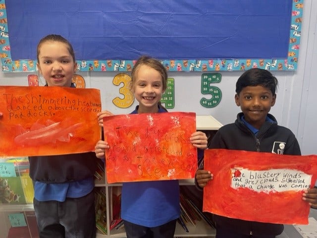 Three students in the classroom holding artwork that they have created